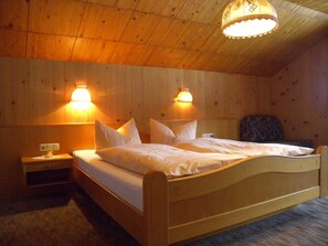 Ein Zimmer mit Holzboden, einem Bett, zwei Wandleuchten, einem Nachttisch und einem Sessel.