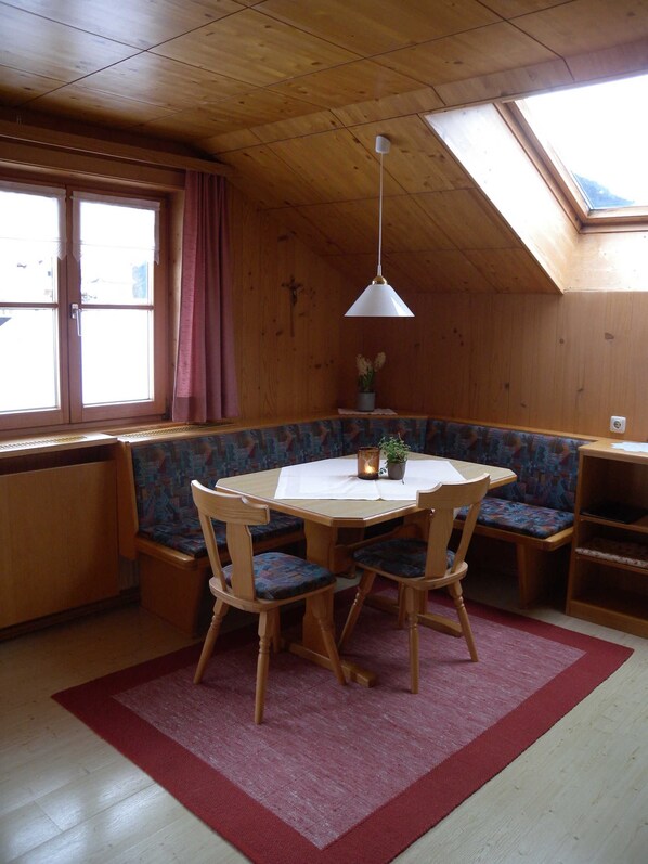Un cuarto acogedor con techo de madera, una mesa redonda con sillas, un banco, un radiador y un tragaluz.