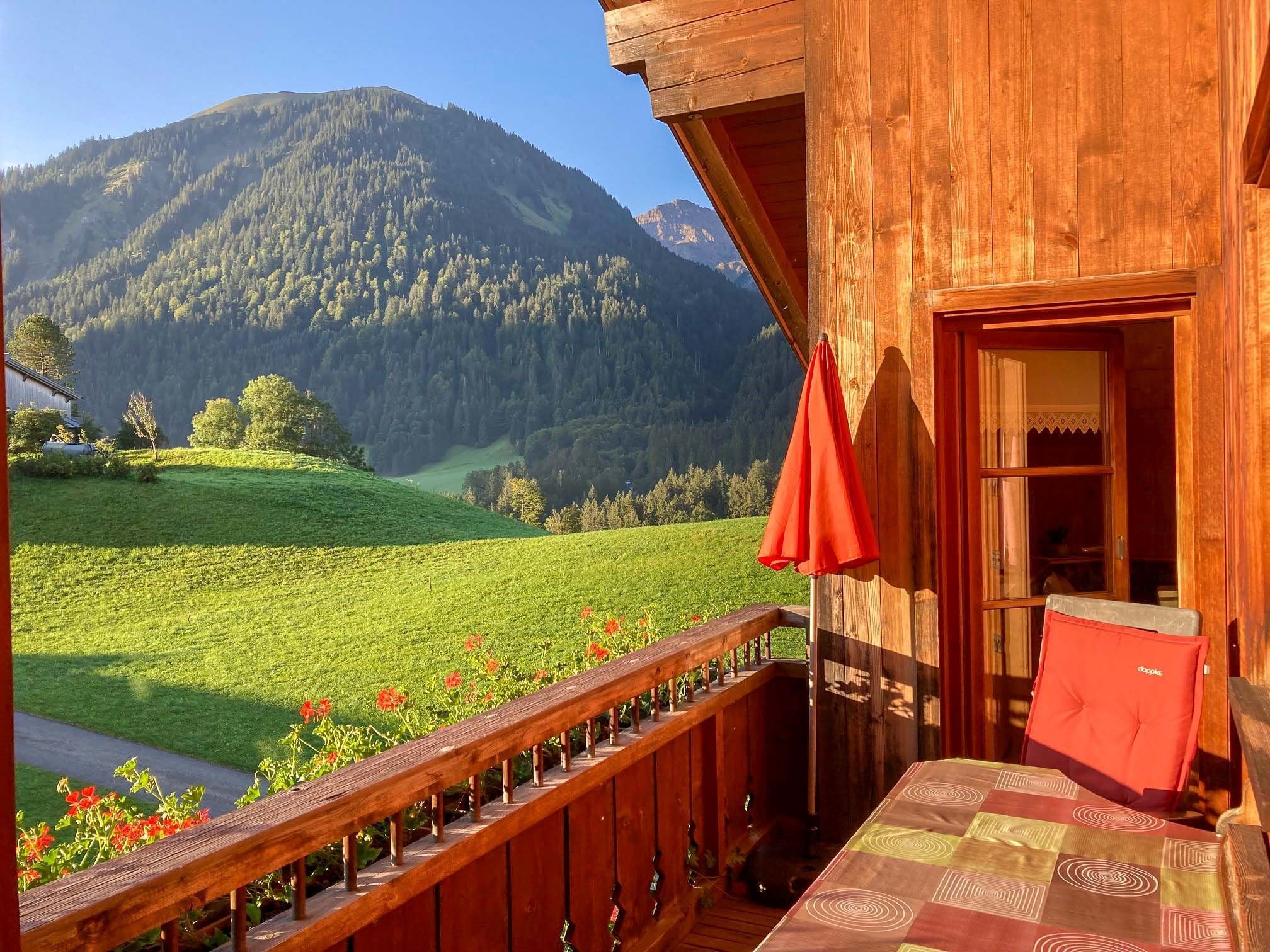 A wooden cabin with a balcony overlooking a green valley and mountains.