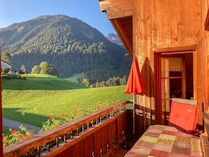 A wooden cabin with a balcony overlooking a green valley and mountains. - Apartment Üntschenspitze - Apartments Haus Monika (Rehmen)