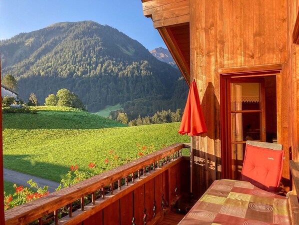 A wooden cabin with a balcony overlooking a green valley and mountains.