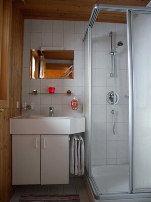 Un baño con cabina de ducha de vidrio, un lavabo blanco y un espejo sobre el lavabo.