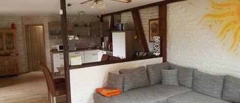 Een woonkamer met een grijze bank, houten vloer en een keuken op de achtergrond.