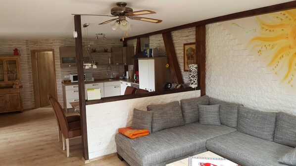 A living room with a grey sofa, wooden floor, and a kitchen in the background. - Apartment Gold - Ferienhof Gold (Waischenfeld)