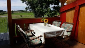 A covered outdoor seating area with a table and chairs, a vase with sunflowers, and a view of a green field.