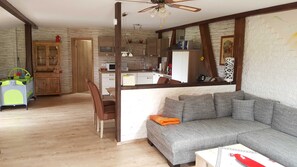 A living room with a grey sofa, wooden floor, and a dining area with a wooden cabinet and a small table.