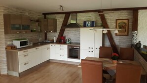 Une cuisine compacte avec des meubles blancs, un four à micro-ondes, une cuisinière et un coin repas comprenant une table et des chaises.