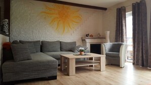 Un salon comprenant un canapé d’angle, une table basse, une cheminée et une grande fenêtre avec des rideaux.