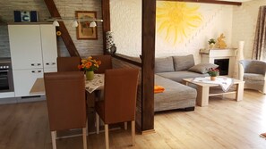 A modern living room with a sofa, a dining table with chairs, a kitchen area with cabinets, and a fireplace.