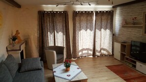 A living room with a sofa, a coffee table with a flower vase, a television, and a fireplace with a decorative rabbit. - Apartment Gold - Ferienhof Gold (Waischenfeld)
