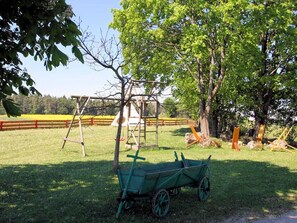 A green wagon, a wooden swing set, and a tree in a grassy field. - Apartment Gold - Ferienhof Gold (Waischenfeld)