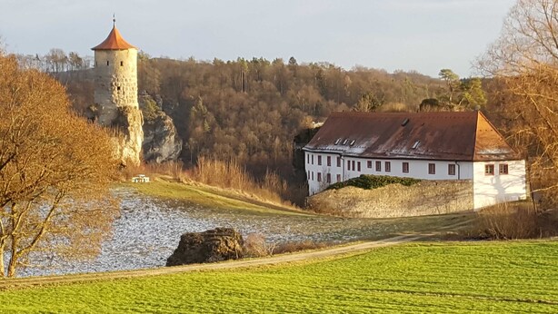 Un château avec une tour, un bâtiment blanc avec un toit rouge, et une rivière au premier plan.