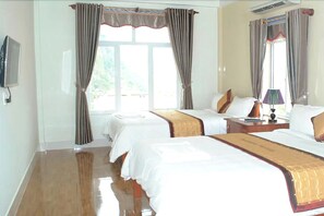 A hotel room with two beds, a flat-screen TV, a bedside table with a lamp, and a window with curtains. - Paradise Hotel (Phong Nha)