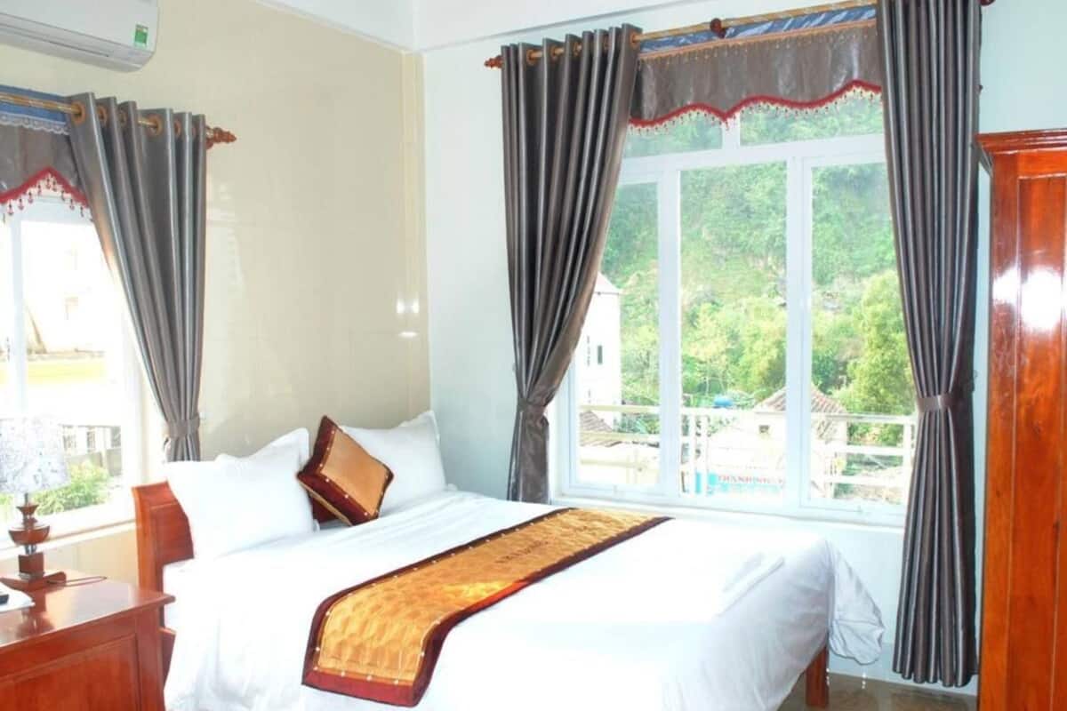 A hotel room with a bed, curtains, a window with a view, and a wooden dresser.