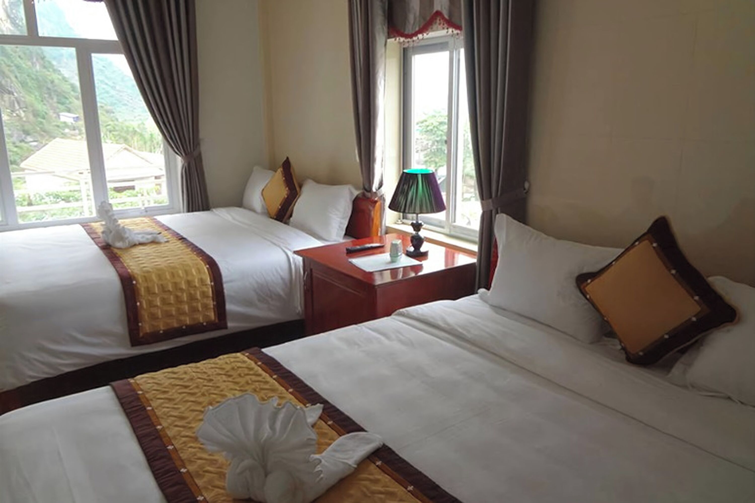 A hotel room with two beds, a nightstand, a lamp, and a view of greenery outside.