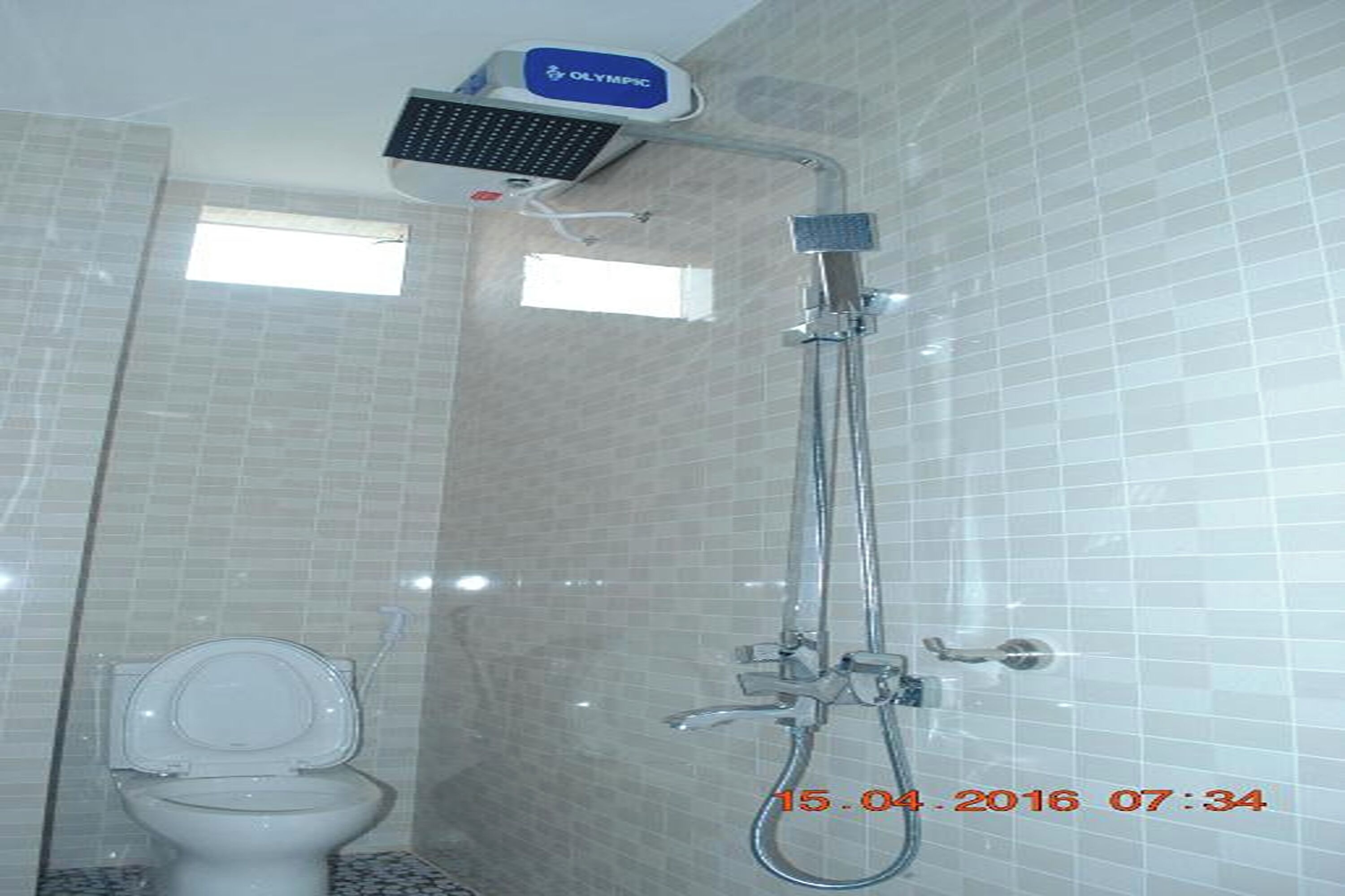 A bathroom with a toilet, a shower with a handheld showerhead, and a wall-mounted faucet.