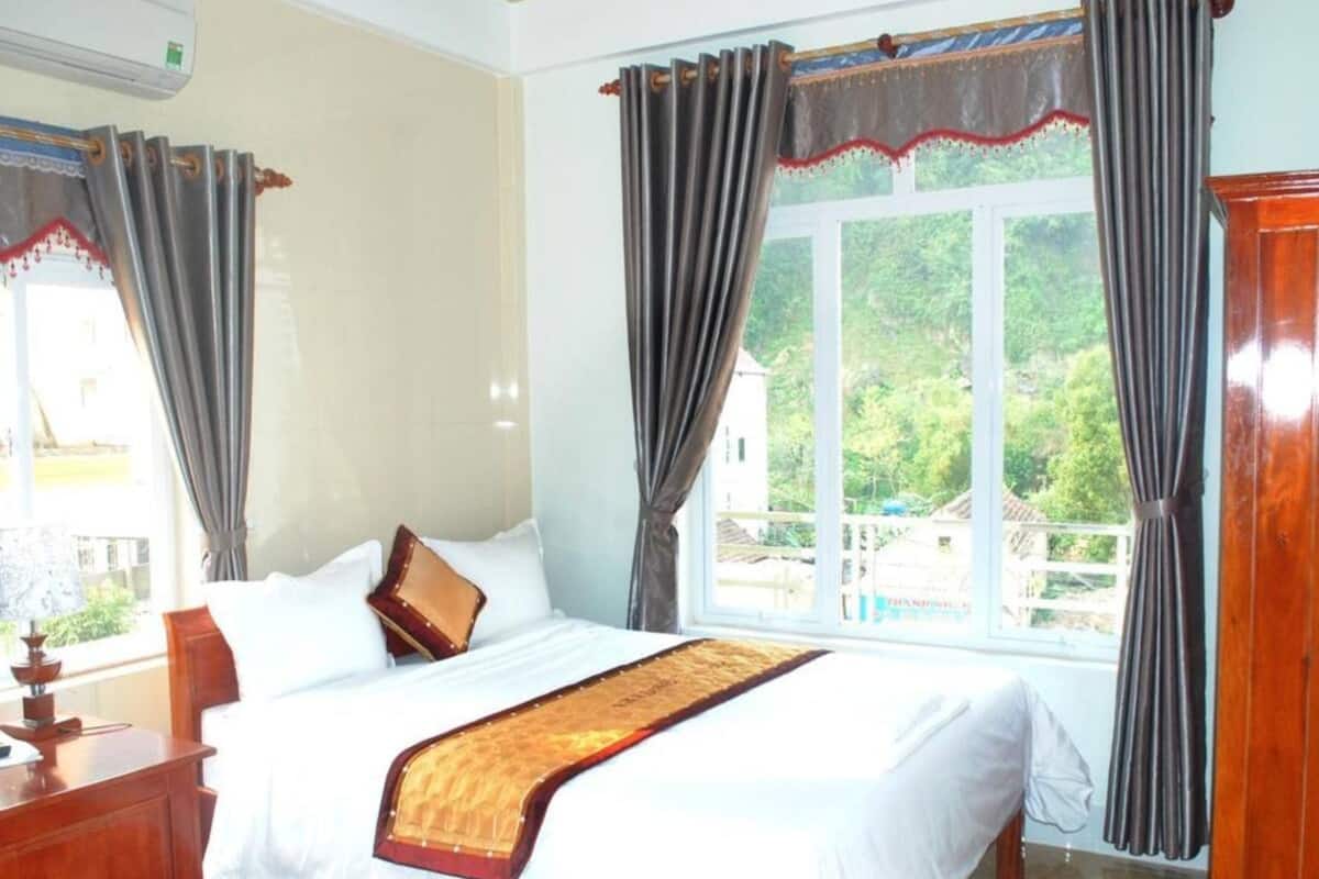 A bedroom with a bed, curtains, a window, and a view of greenery outside.
