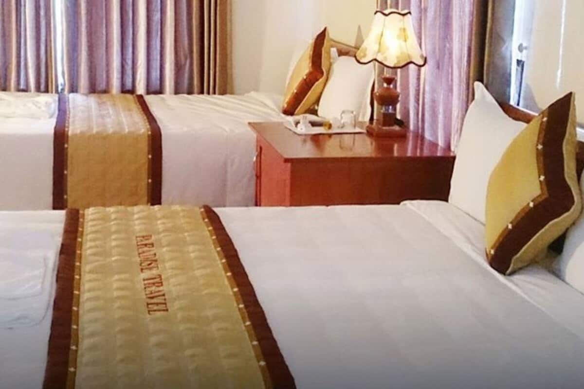A hotel room with two beds, a nightstand, a lamp, and curtains.
