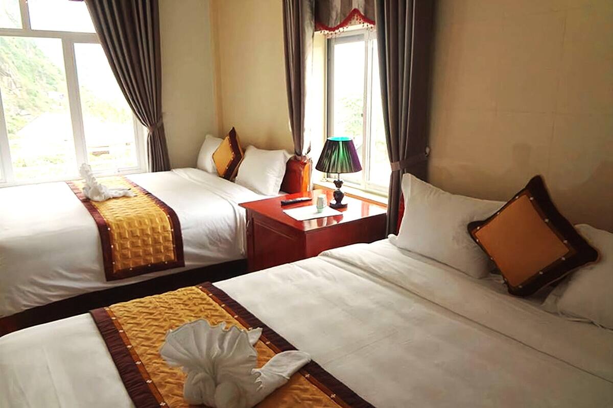 A hotel room with two beds, a nightstand, a lamp, and a window with curtains.