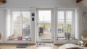 A room with a large window, a door leading outside, and a view of a balcony with outdoor furniture.