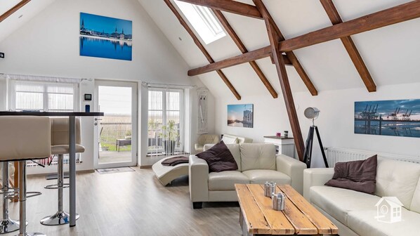 A spacious living room with a high ceiling, wooden beams, a balcony with a view, and modern furniture.