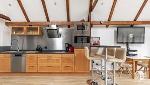 Una cocina moderna con armarios de madera, electrodomésticos de acero inoxidable y una zona de comedor con taburetes de bar.