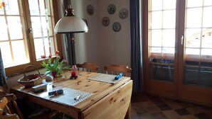 A wooden dining table with chairs, a lamp, a vase with flowers, and a window with curtains. - Chalet Blettner, Switzerland (Randa VS)