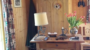 A wooden interior with a chandelier, a wooden table with a lamp, a vase with tulips, and a patterned rug. - Chalet Blettner, Switzerland (Randa VS)