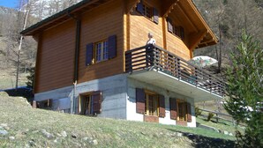 A wooden chalet with a balcony, a stone foundation, and a mountainous backdrop. - Chalet Blettner, Switzerland (Randa VS)