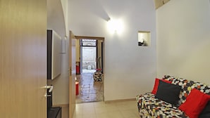 Un salon avec un canapé, un téléviseur et une porte donnant sur un couloir.