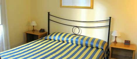 A single bed with a striped bedspread, a headboard with a circular design, two bedside tables with lamps, and a framed picture on the wall.