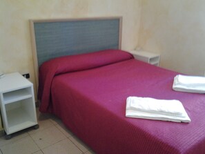 A single bed with a red bedspread and white pillows, a white nightstand, and a white shelf unit. - Luna B&B (Rome)