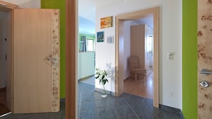 Un couloir avec une porte en bois, un mur vert et un sol carrelé.