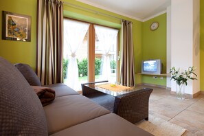 A living room with a sofa, a table, a flat-screen TV, and a window with curtains. - Top 1 - 3 (2) - Apartment block Charisma (Fieberbrunn)
