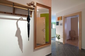 A hallway with a wooden door, a mirror, a hanging umbrella, and a chair. - Top 1 - 3 (2) - Apartment block Charisma (Fieberbrunn)