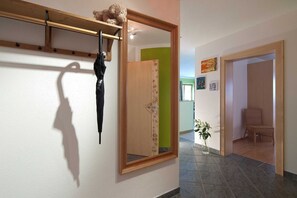 A hallway with a large mirror, a wooden shelf with a teddy bear, a potted plant, and a wicker chair. - Top 1 - 3 (2) - Apartment block Charisma (Fieberbrunn)
