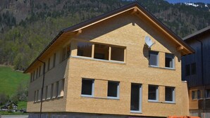 Una casa de madera de dos pisos con techo inclinado, ventanas grandes y una antena parabólica.
