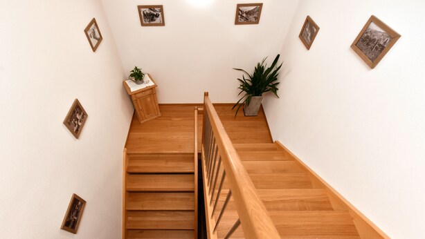 Una escalera de madera con barandilla, paredes blancas y varias fotografías enmarcadas.