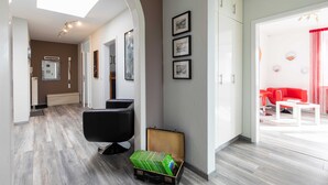 Un moderno vestíbulo de hotel con piso de madera, un sillón de cuero negro, una maleta y un sofá rojo al fondo.