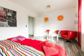 Une chambre d’hôtel moderne avec un grand lit, un fauteuil rouge et une petite table blanche.