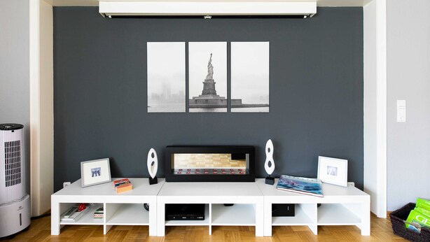 Una sala moderna con un mueble blanco para entretenimiento, un cuadro con una estatua y una chimenea.