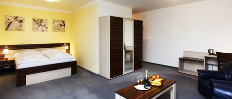 A modern hotel room with a bed, a wooden coffee table with fruits and drinks, a sofa, and a wardrobe.
