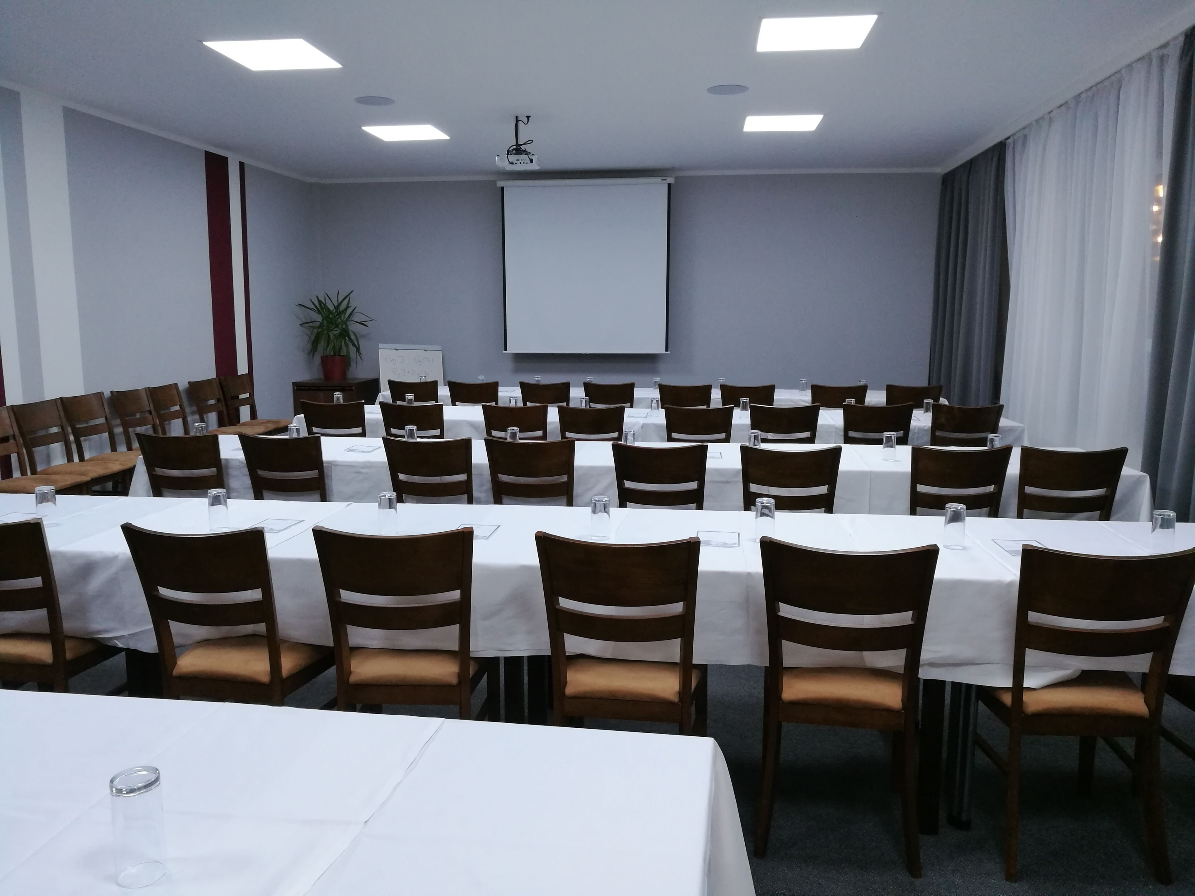 A conference room with multiple tables and chairs, a projector screen, and a whiteboard.