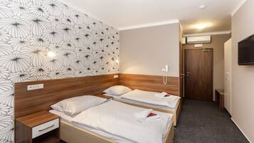 Habitación de hotel con dos camas, cabecera de madera, mesita de noche, televisor montado en la pared y puerta con equipo de aire acondicionado.