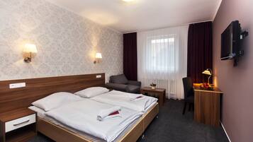 A hotel room with a large bed, two bedside tables, a desk with a chair, a TV mounted on the wall, and a window with curtains.
