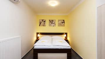 Habitación de hotel estrecha con cama, lámparas de noche y tres cuadros florales colgados en la pared.