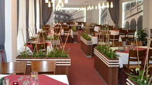 Een restaurant interieur met meerdere eettafels, houten stoelen, hangende hanglampen en potplanten.
