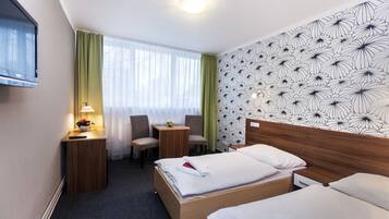 Ein Hotelzimmer mit zwei Betten, einem Schreibtisch, einem Sessel, einem Fernseher und einem Fenster mit Vorhängen.