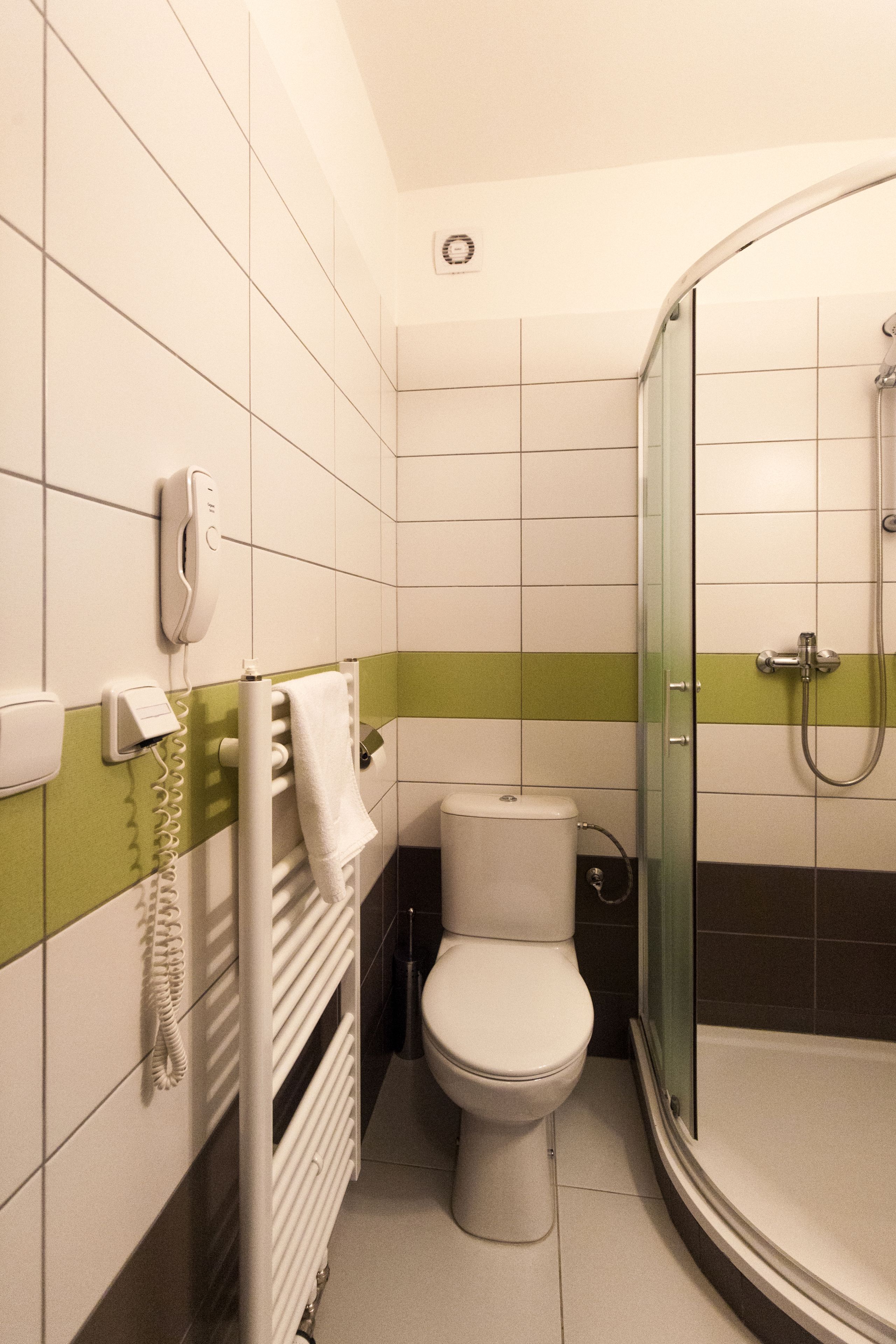 A bathroom with a toilet, a glass-enclosed shower, a towel rack, and a telephone.