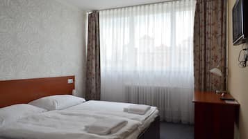 A hotel room with a double bed, a wooden headboard, a desk with a lamp, and a TV on the wall.